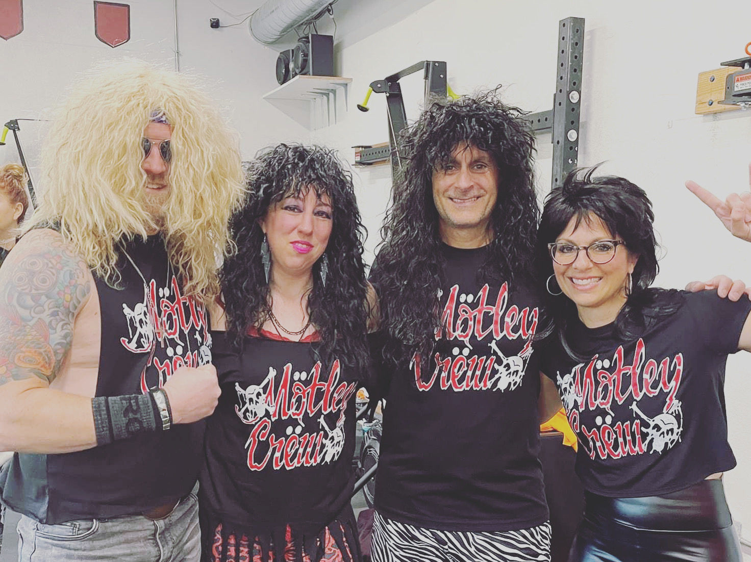 Four people wearing matching black shirts with red and white rock-inspired lettering